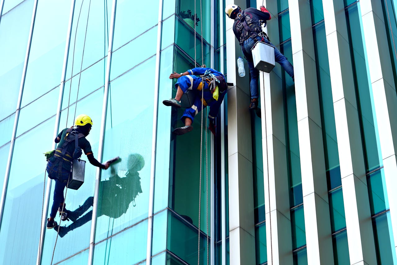 gallery-04 Three window cleaners suspended on ropes clean a modern glass building facade during the day.