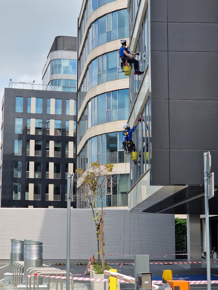 services-03 Two workers clean windows on a tall office building in a city setting.
